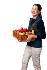 Freudige BioMarkt Mitarbeiterin trägt Korb mit Obst